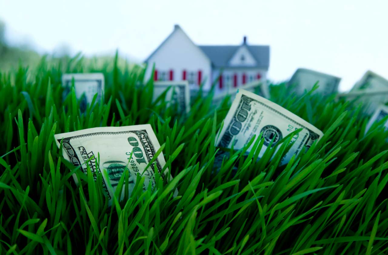 Close-up of hundred-dollar bills in green grass with a house in the background to show hidden savings from an interest rate buydown on San Diego homes for sale